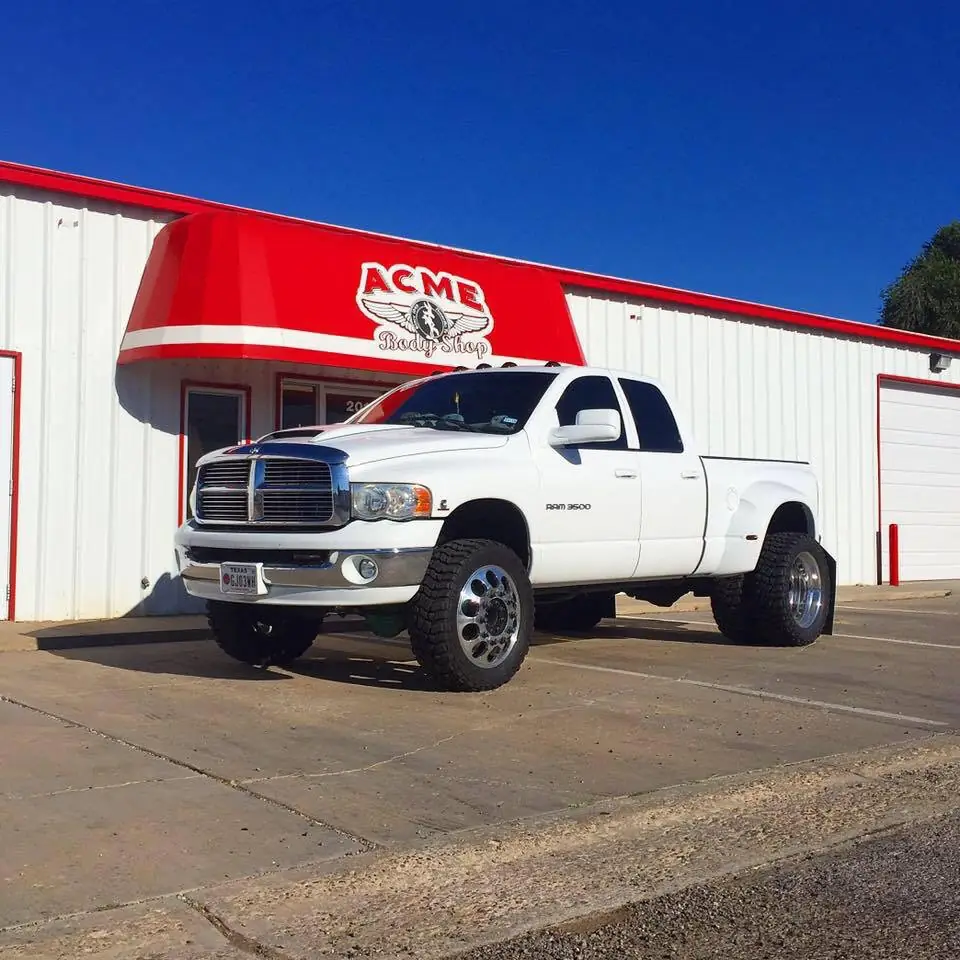 A lifted white Ram dually parked under the red Acme Body Shop awning on Ong Street