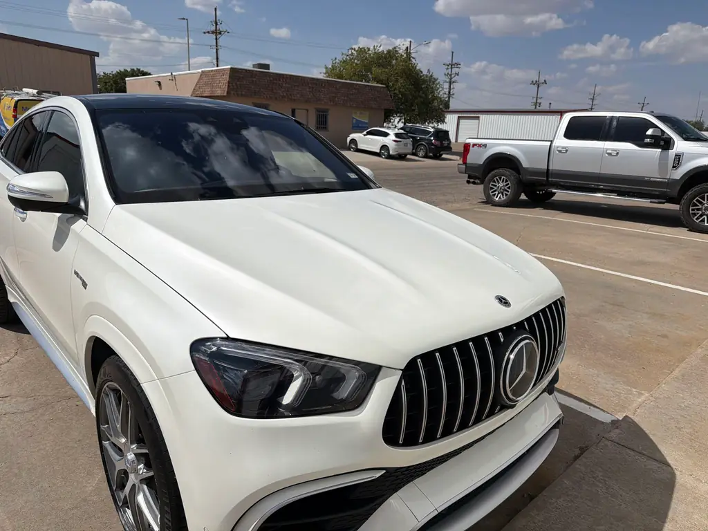 A completed white Mercedes-AMG SUV, front three-quarter, standing in Acme's own lot after a collision repair