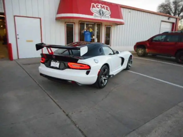 A freshly painted white, black and red Dodge Viper, rear three-quarter, parked in front of the ACME awning entrance